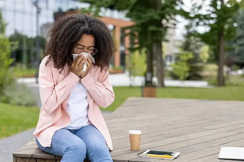 African American woman sneezing while sitting outside