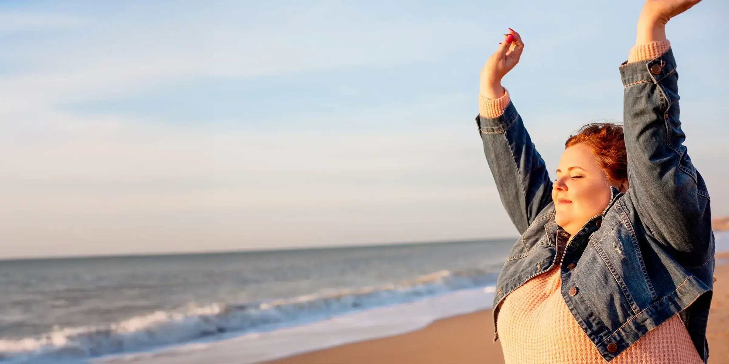 Woman on beach holds hands up to feel wind