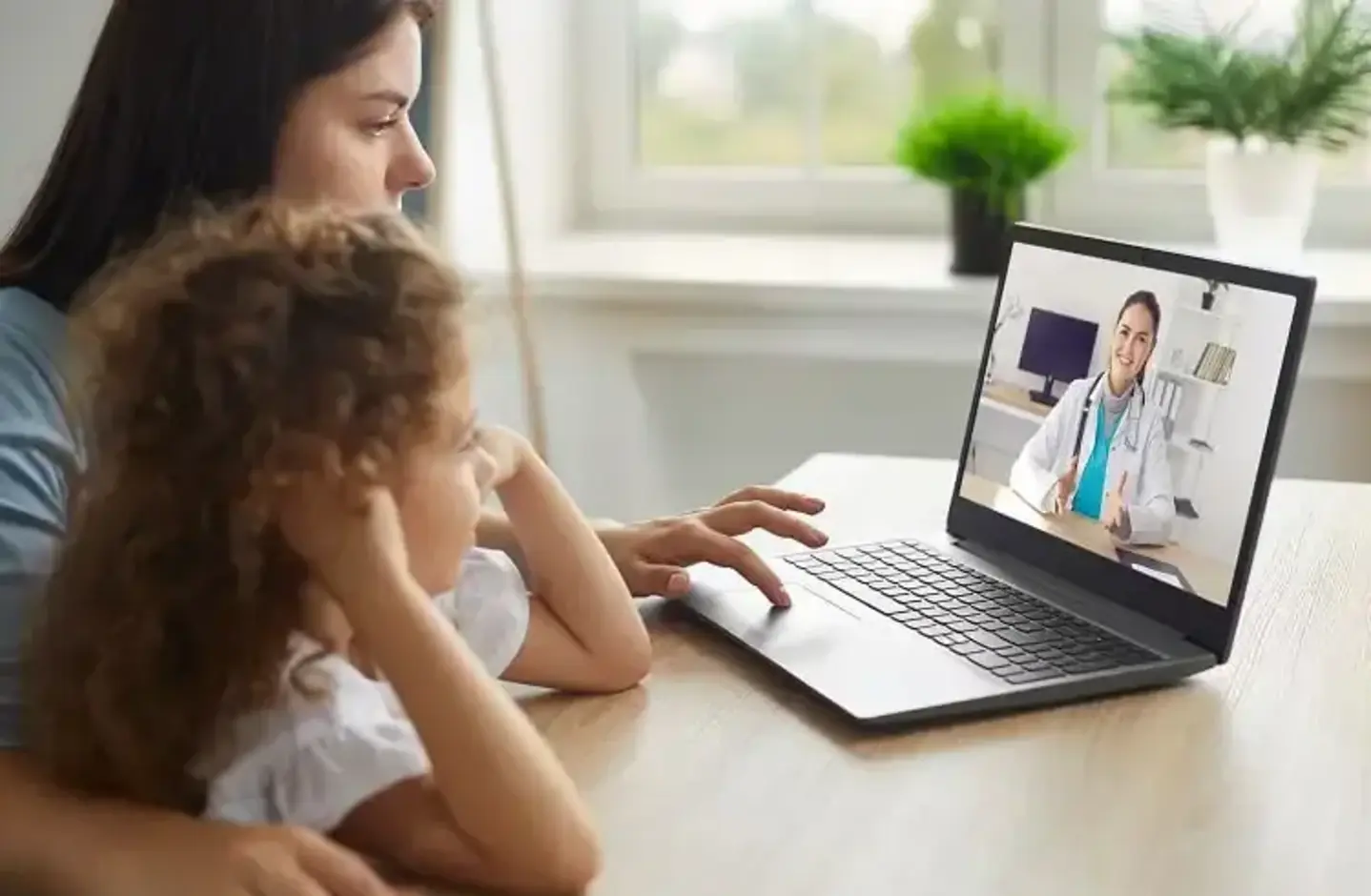 Mother and daughter at home on a laptop during a virtual care appointment with a pediatrician.