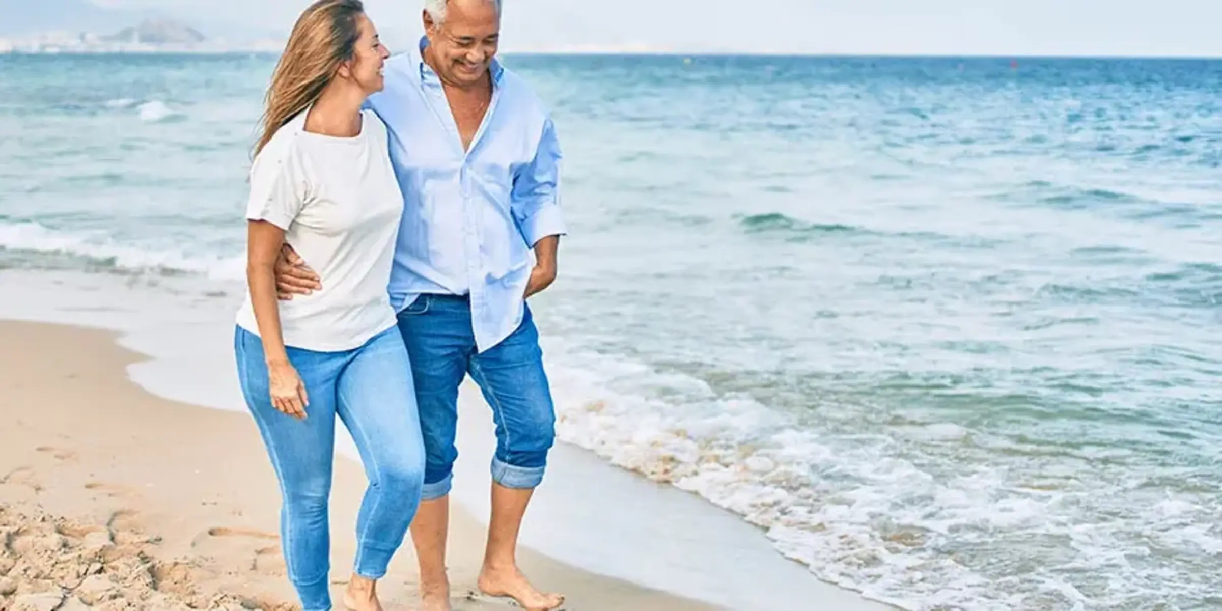 Middle age hispanic couple smiling happy and hugging walking at the beach.