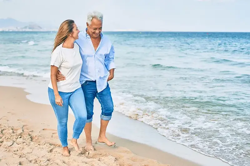 Middle age hispanic couple smiling happy and hugging walking at the beach.