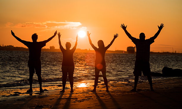 Adults with hands in air on beach at sunset